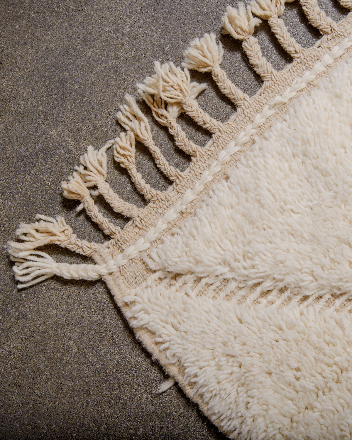 Corner of cream Beniourain rug with natural wool tassels.